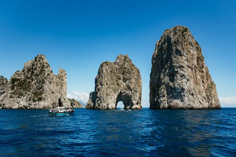 A boat passing the three Faraglioni sea stacks off Capri