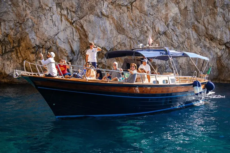 A skipper rowing guests in a small wooden boat beside Capri's cliffs