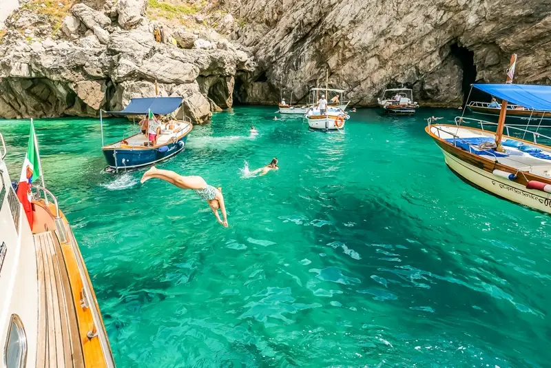 Swimmers diving into a turquoise Capri cove from a tour boat